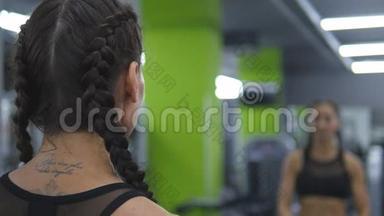 年轻漂亮的女人在健身房训练，在镜子前举起和放下哑铃。 体育健身女孩